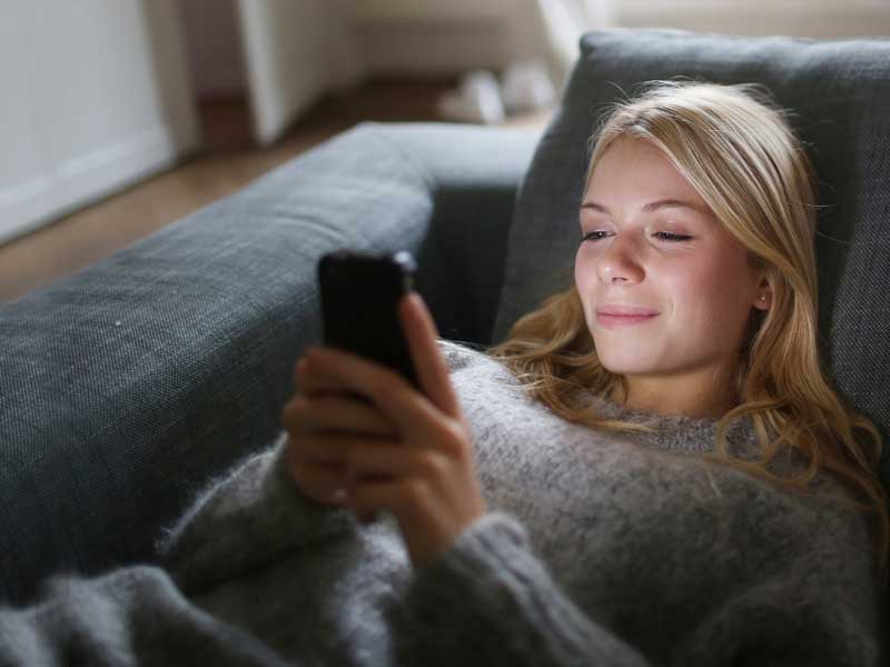 Une femme allongée dans un canapé utilisant son smartphone